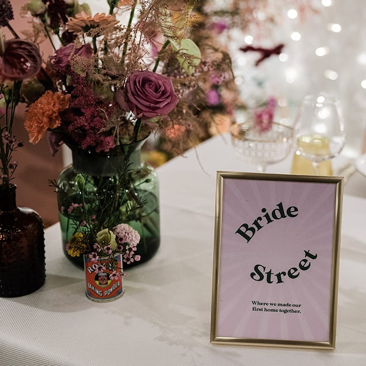Purple table name sign in gold photo frame on tables with white tablecloths and lilac napkins