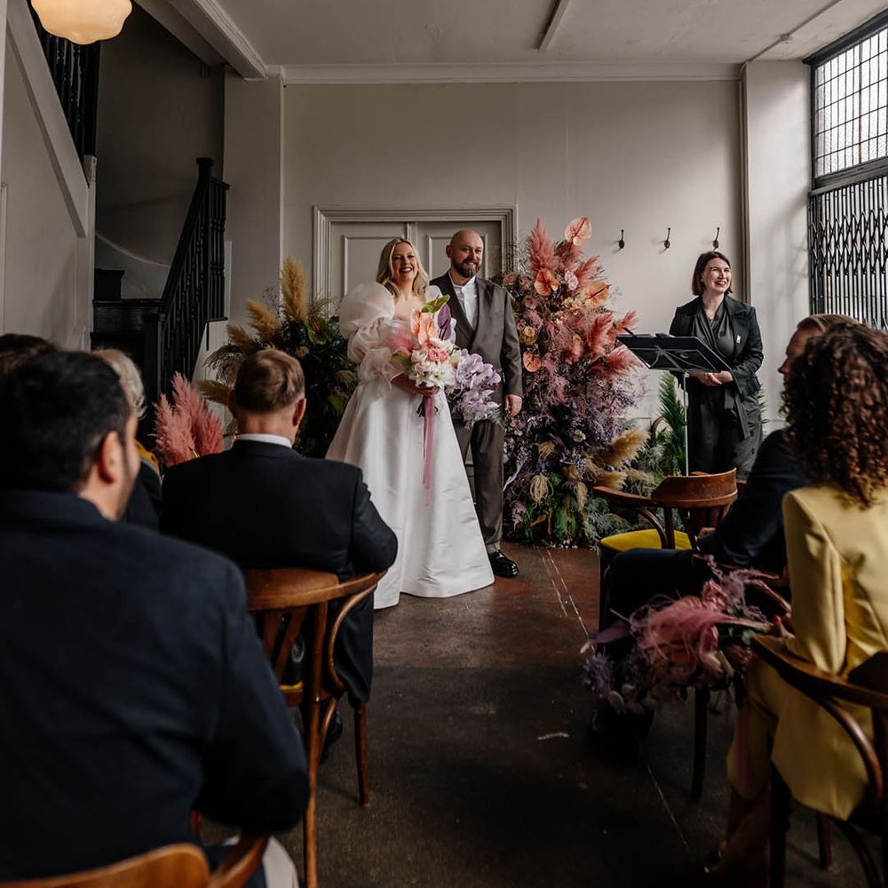 Floral Hall humanist wedding ceremony with column flowers at the altar, bride in a JESUS PEIRO wedding dress and groom a double breasted jacket