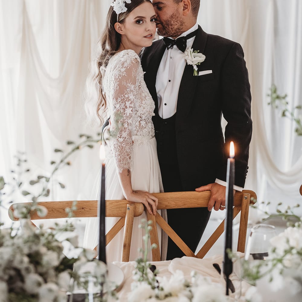 Groom in black tie leans into the bride as she looks at the camera for their wedding at Willow Grange Farm