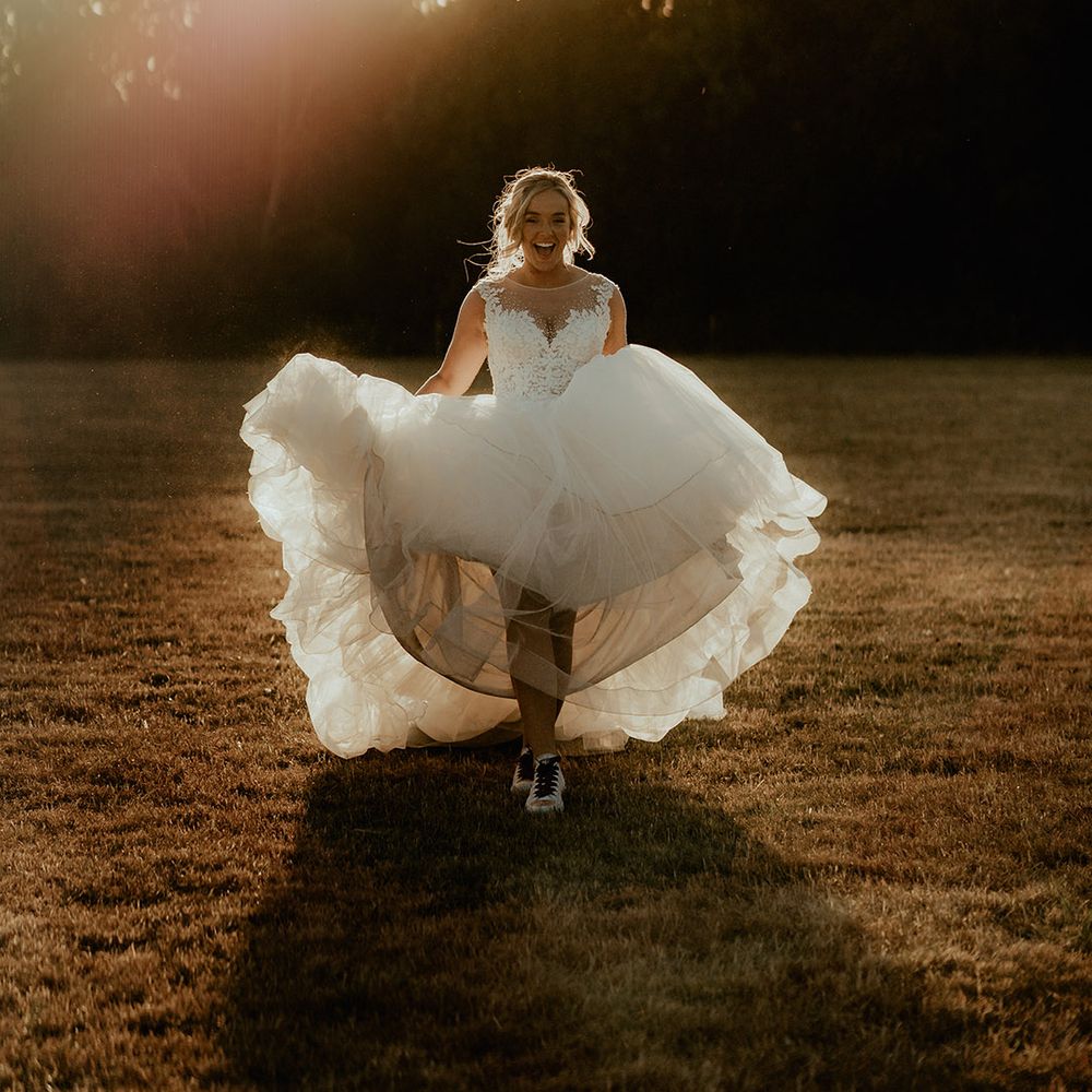 Bride in a princess wedding dress runs during the sunset with personalised Converse shoes 