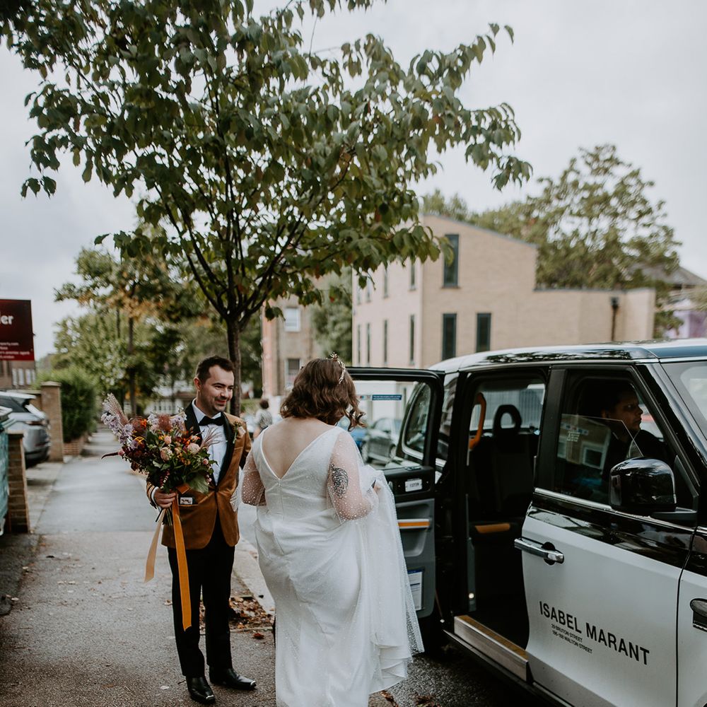 Groom holds Bride’s bouquet as she lifts her Dig For Victory Celestial wedding dress up to get into taxi