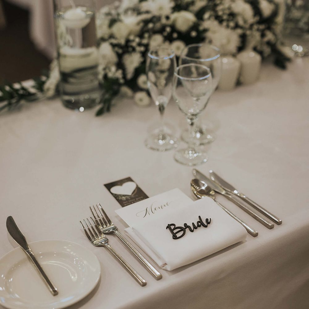 Classic and clean all white wedding tablescape with personalised laser cut place names with silver cutlery and white flowers