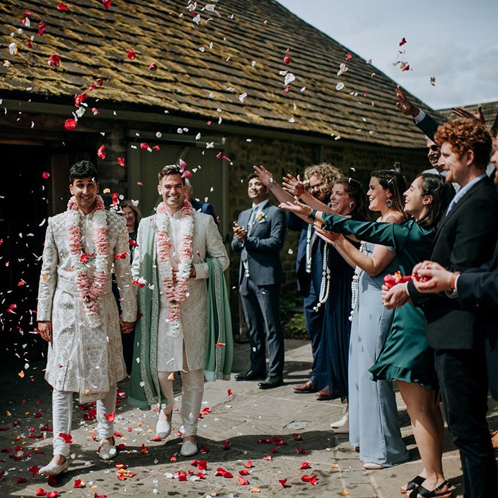 Grooms in matching colourful lei's walk through confetti petals outdoors after wedding ceremony