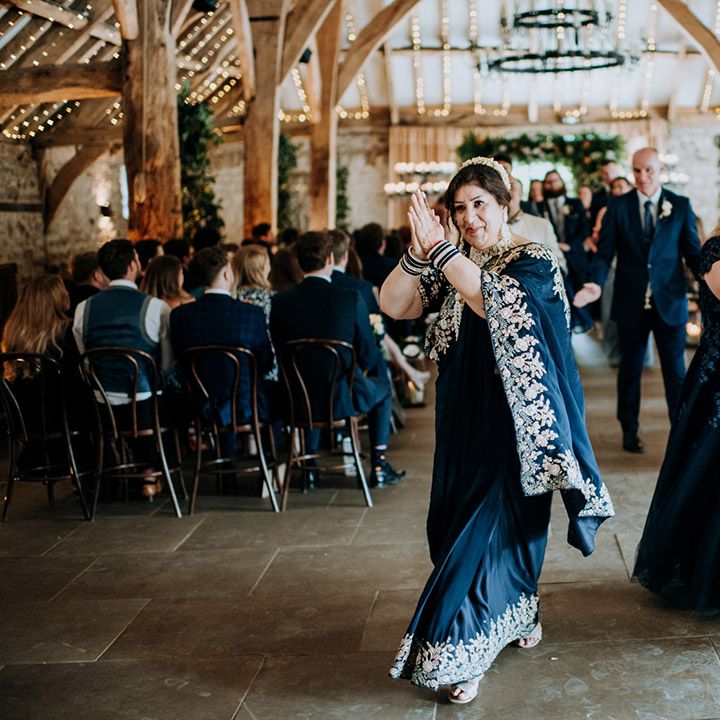 Wedding guests in deep blue dance during barn wedding ceremony for multicultural wedding day