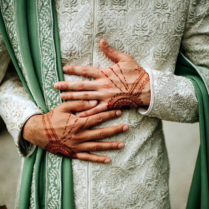 Grooms hands complete with henna wrapped around white and sage green sherwani 