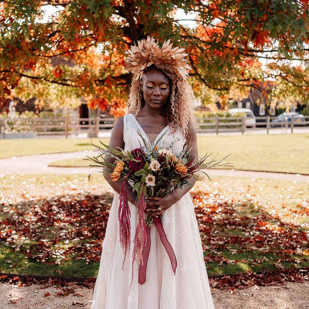 Bride in star embroidered peach floaty wedding gown holding autumnal dried flowers and large golden bridal crown 