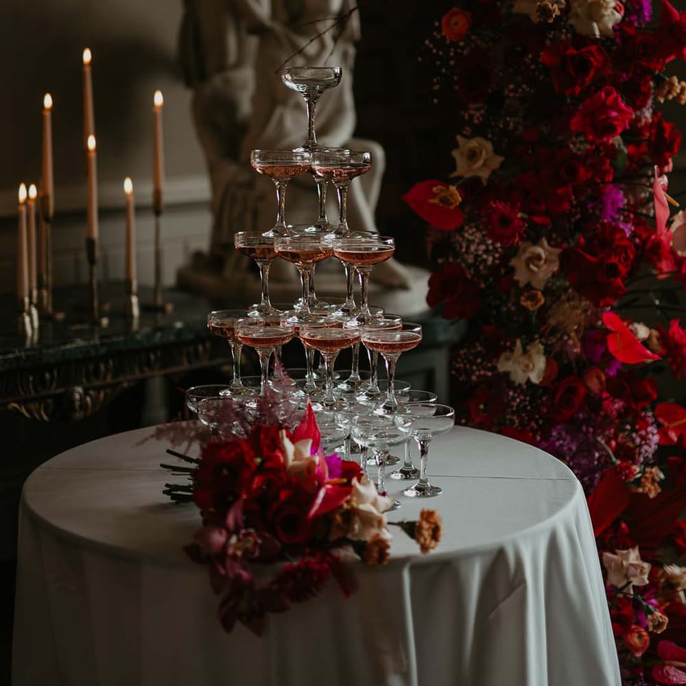 Pink Champagne tower at rock and roll meets disco wedding with large magenta floral displays and tapered off white candles in gold candlestick holders