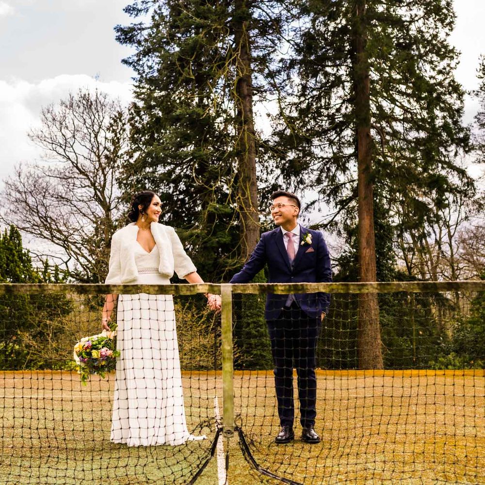 Bride wears faux fur coverup and stands beside her groom during outdoors couples portraits 