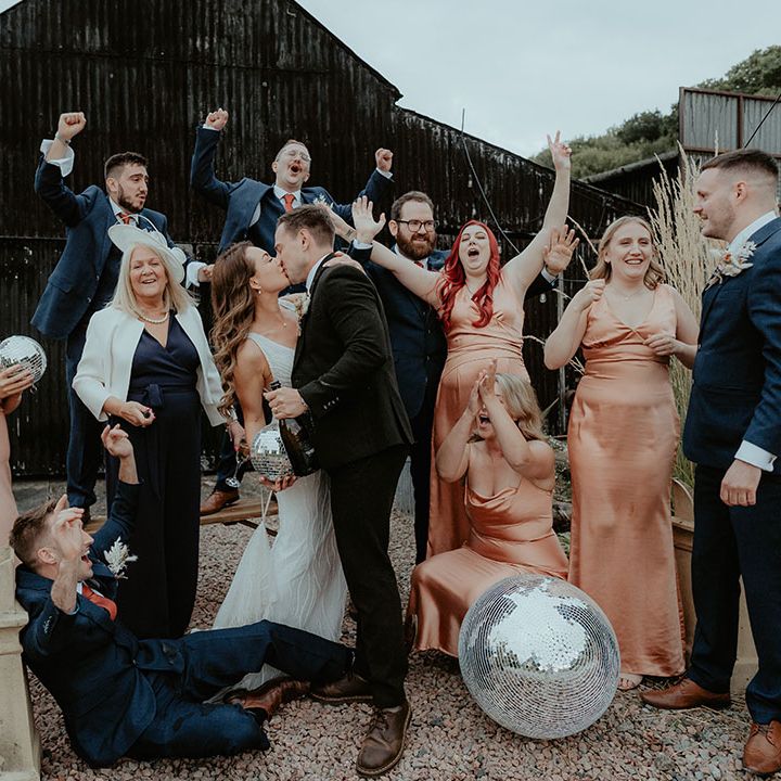 Epic wedding party photo of the bride and groom kissing surrounded by their bridesmaids and groomsmen with disco ball decor 