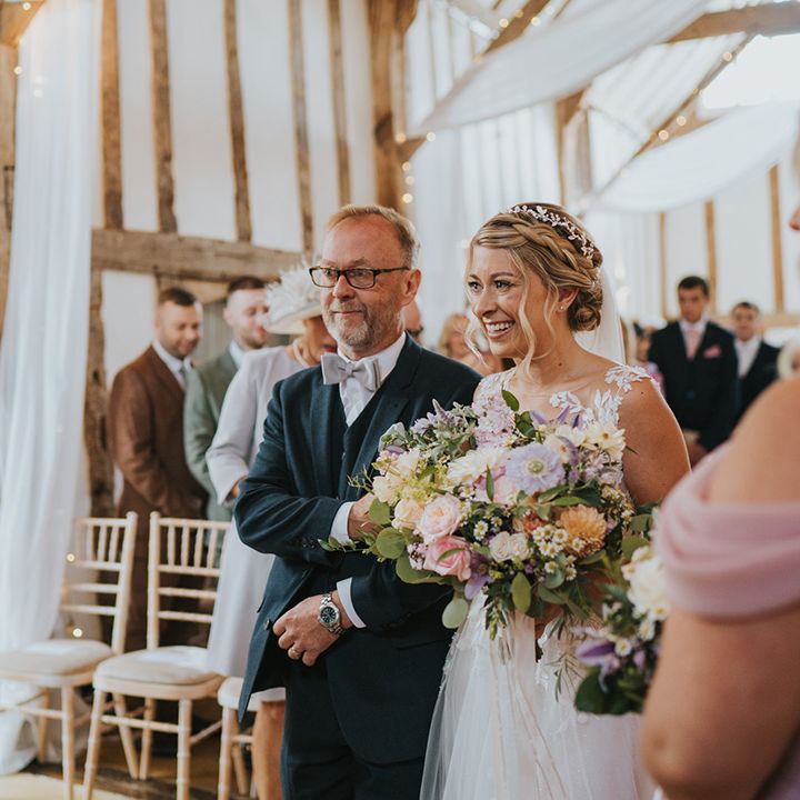 Father of the bride in navy suit with grey bow tie walking bride in illusion lace Dando London wedding dress to the groom holding their son 