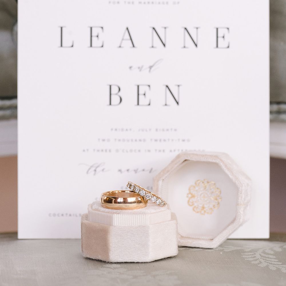 The groom's thick plain gold wedding band and the bride's diamond and gold wedding band in velvet ring box in front of the black and white wedding stationery