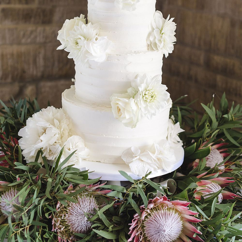 Three tier white iced wedding cake with white wedding flower decorations on white cake stand 