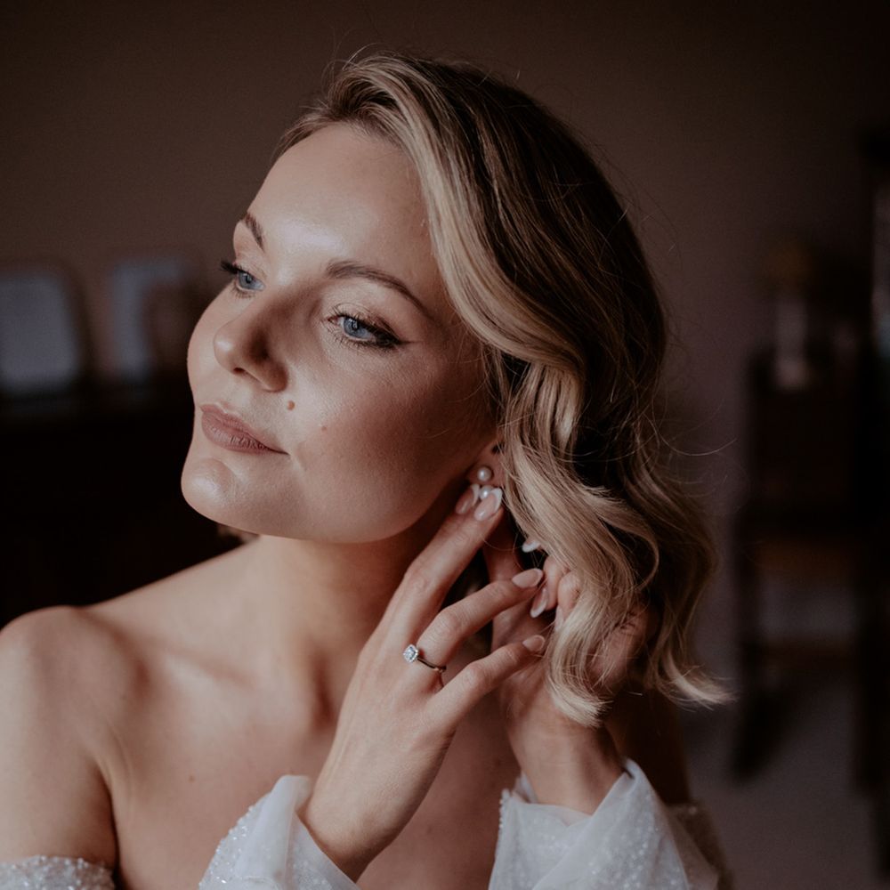 Bride with white French tip classic wedding nails puts in her pearl earrings for the wedding in a sparkly wedding dress 