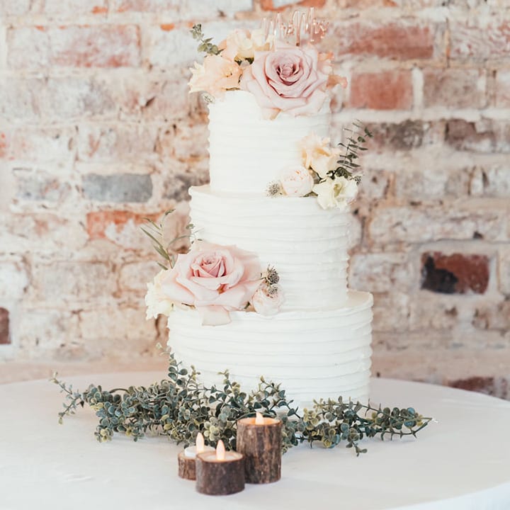 Three tier white wedding cake with pink rose wedding cake decoration with foliage details