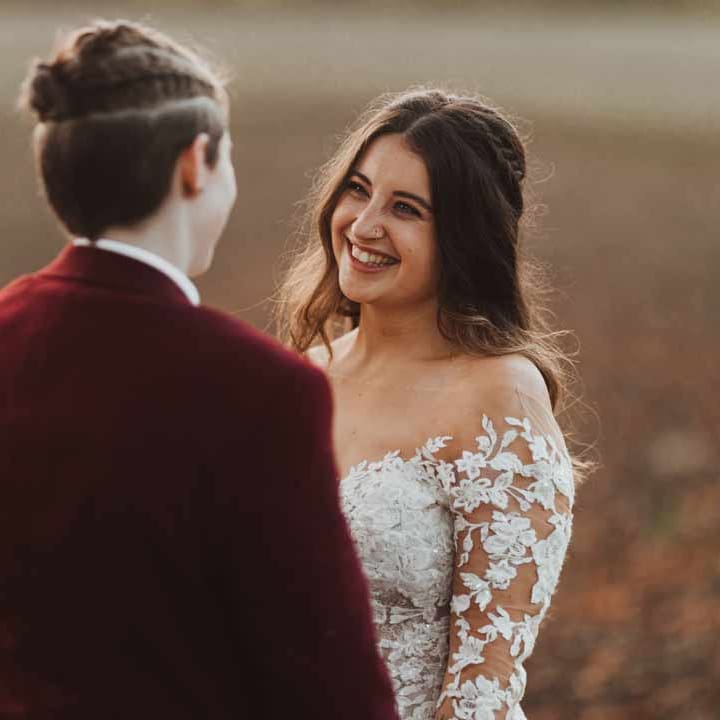 Bride in maroon bridal suit with bride in long sleeve lace illusion sleeve wedding dress with overlay 