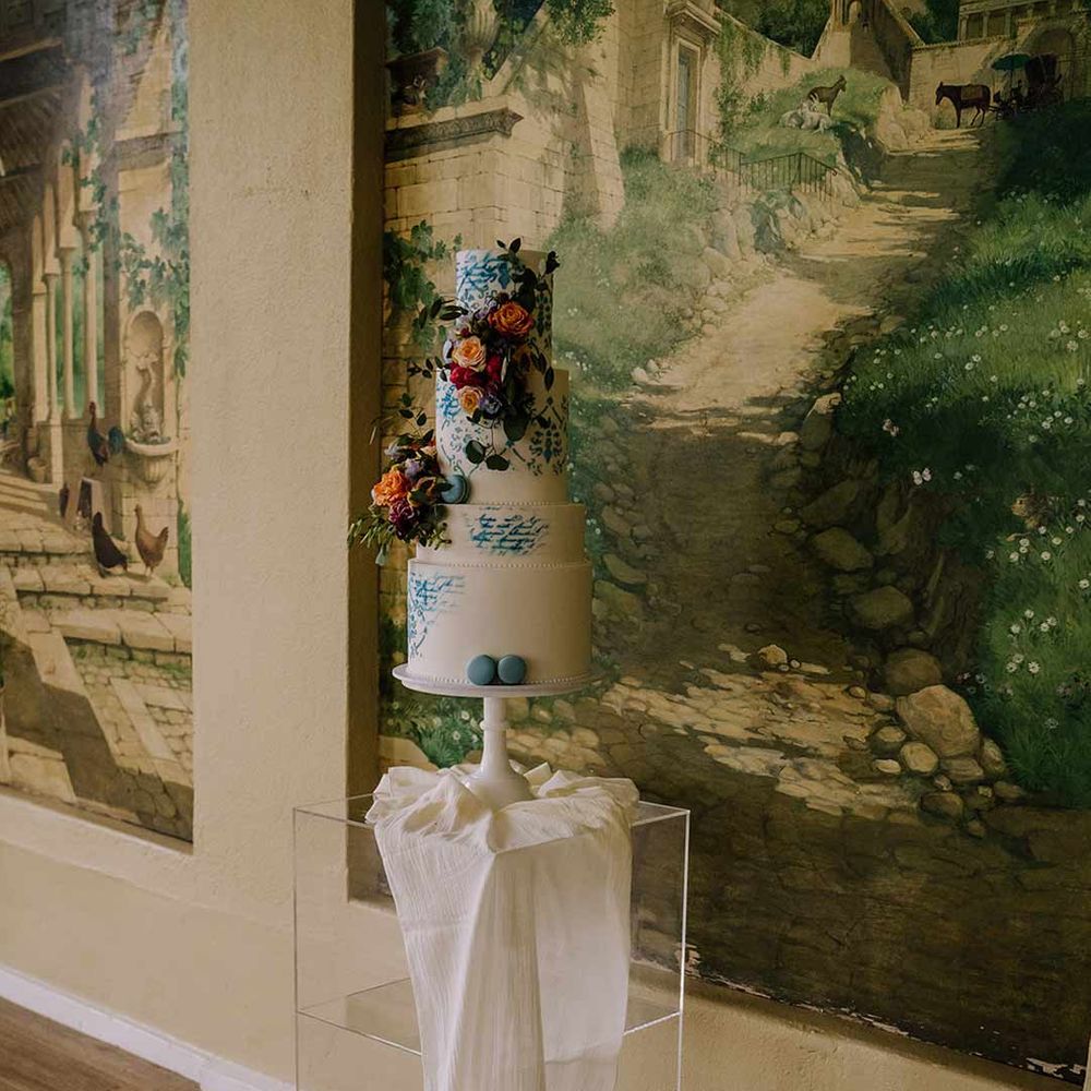Four tiered toile wedding cake with white and blue icing and spring floral wedding cake toppers with blue macaroons 