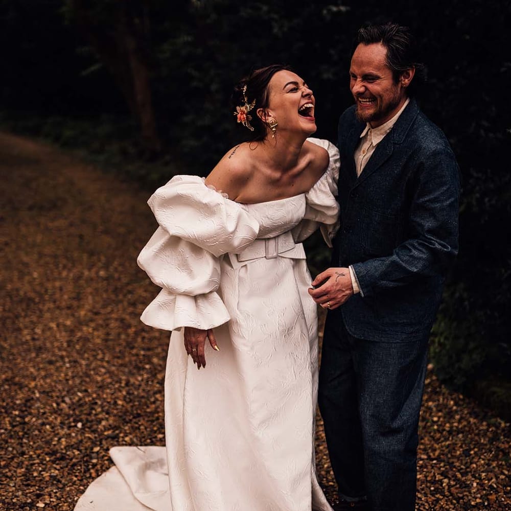 Bride in Jesus Peiro wedding dress smiling for couple photos with the groom in a denim suit and hat 