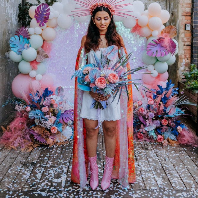 Stylish bride in short dress, cape, boots and crown at festival wedding 