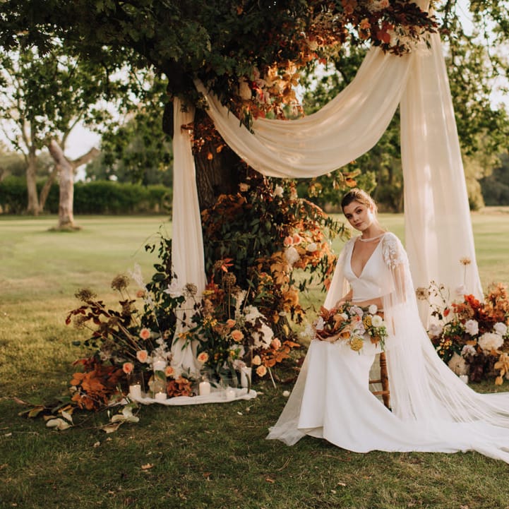 Bride sitting at a floral altar in the grounds of Reymerston Hall