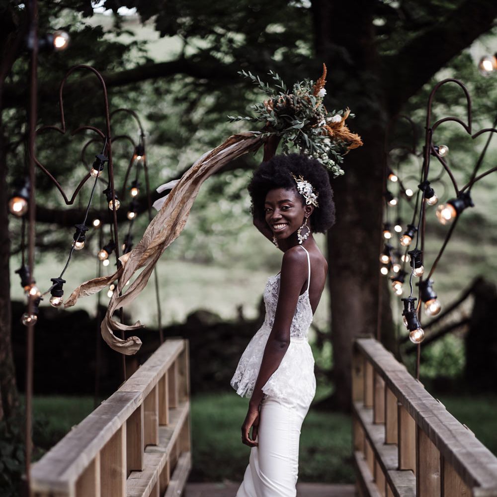 Bride in a fitted wedding dress standing on a bride at Ponden Mill smiling 