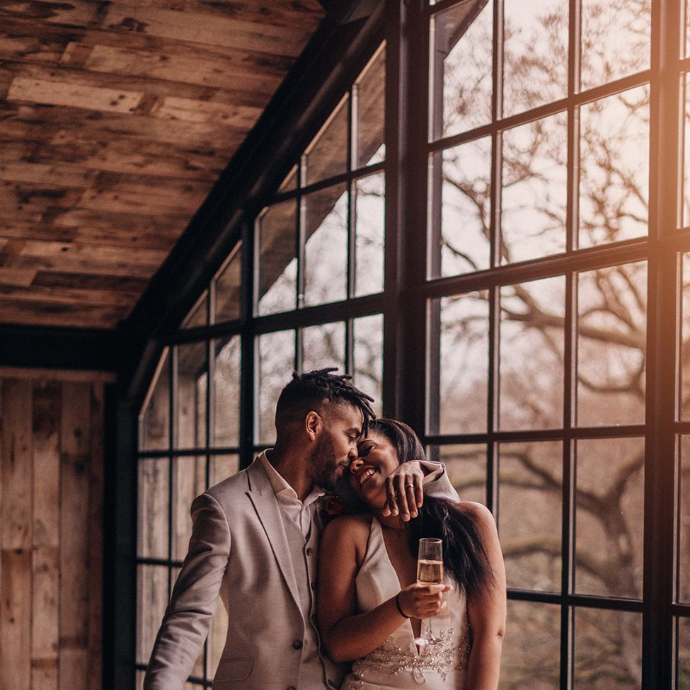 Bride & groom laugh as bride holds glass of champagne and floral bouquet 