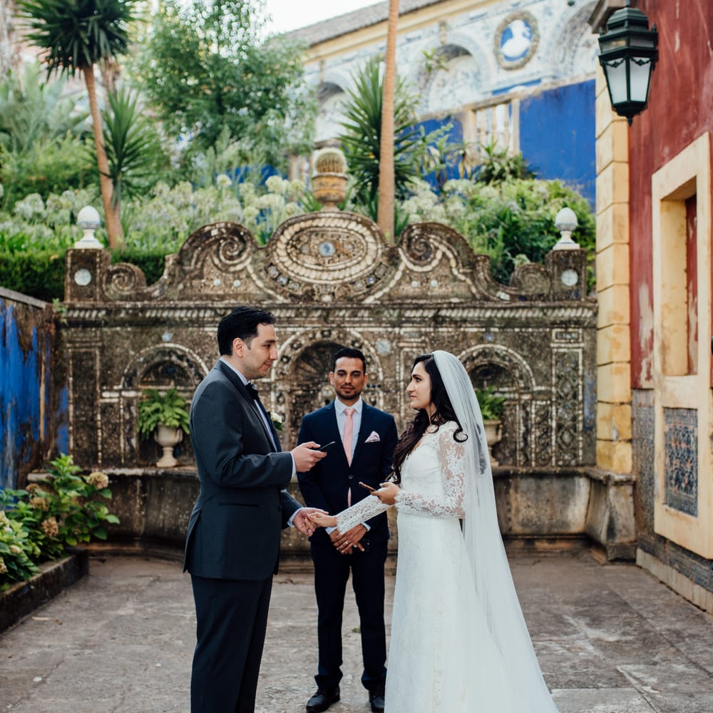 Bride & groom hold hands and look lovingly at one another during wedding ceremony outdoors