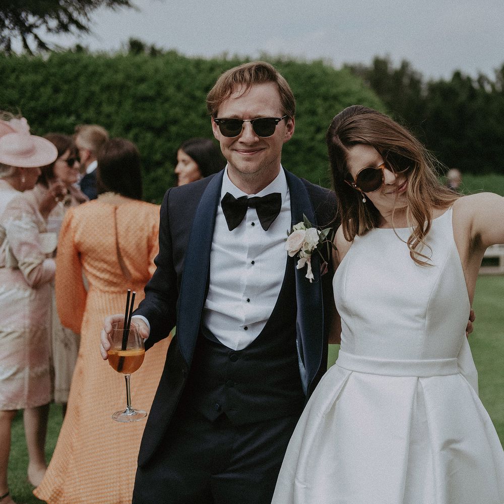 Bride & groom wear sunglasses outdoors on their wedding day as they celebrate with friends