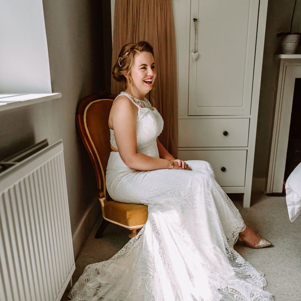 Bride laughs whilst wearing red lipstick and holding her hands in her lap on the morning of her wedding