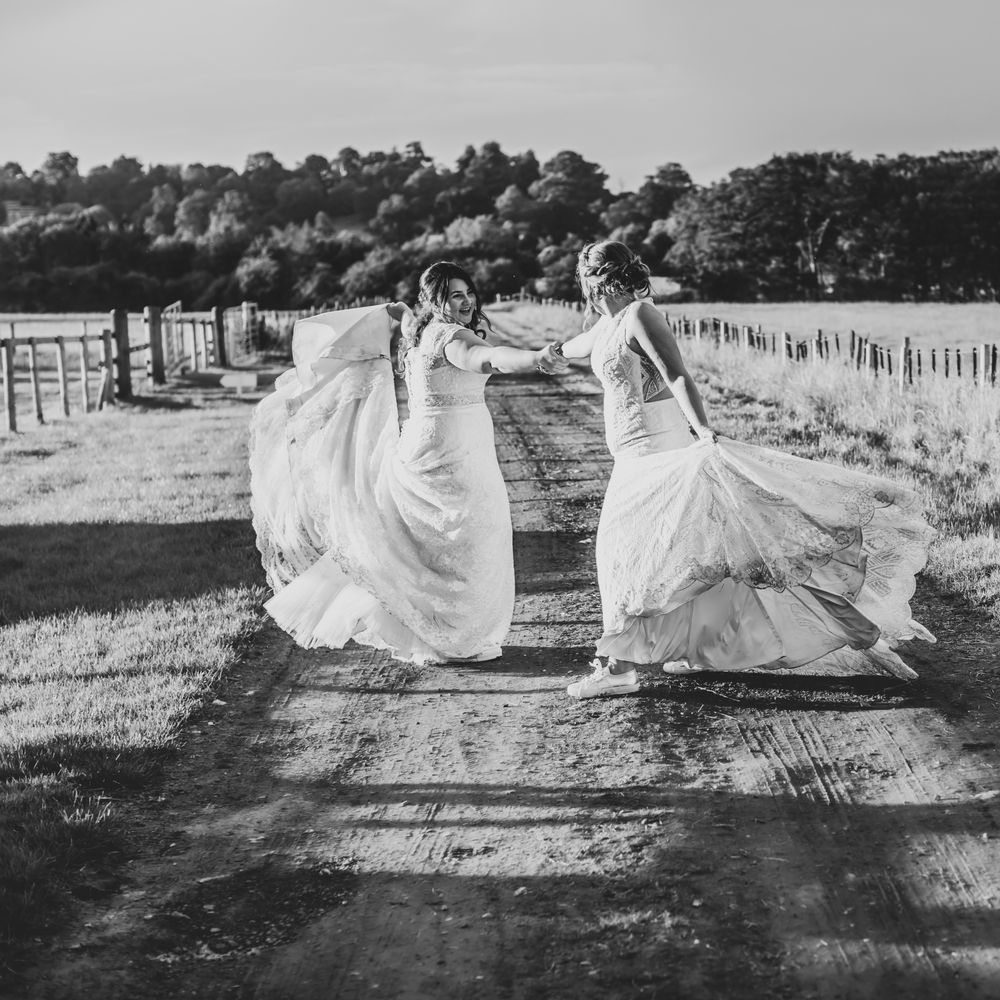 Brides hold hands and dance together through the countryside for Park Farm wedding