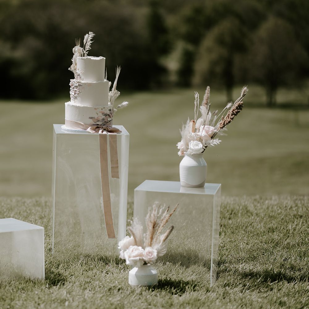 Three tier buttercream wedding cake decorated with dried flowers and grasses resting on a perspex plinth 