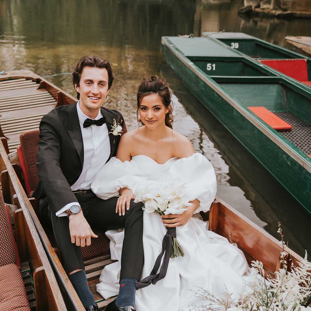 Stylish bride and groom in a tuxedo and Nortier Shallow wedding dress sitting on a boat at their Oxford wedding 