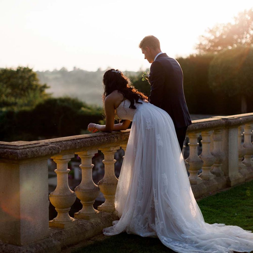 Bride leans across wall as the sun begins to set on her wedding day