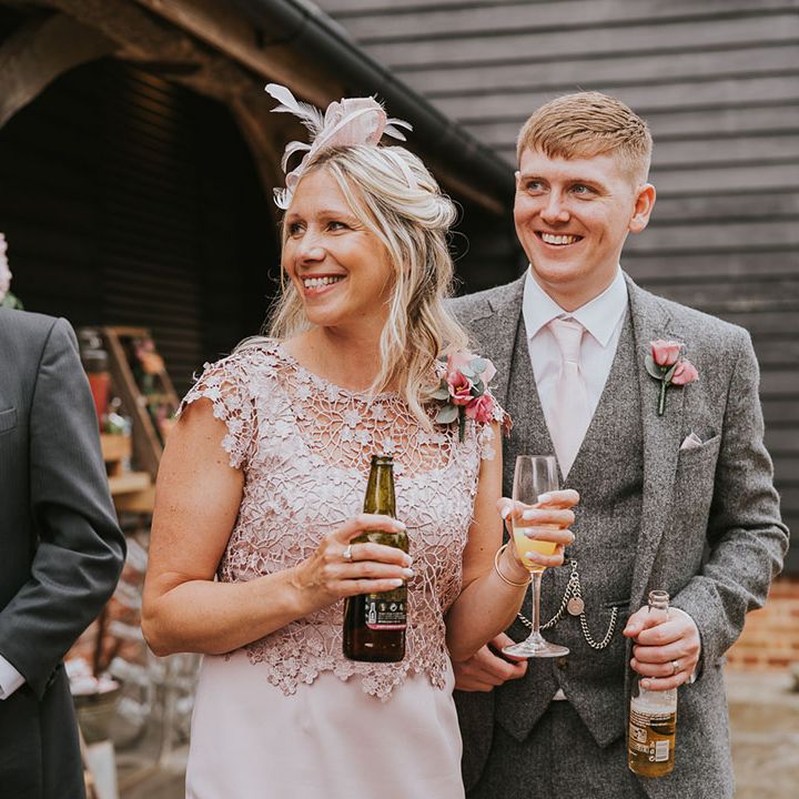 Groomsman in matching grey tweed suit with wedding guest in bliss pink dress and fascinator 