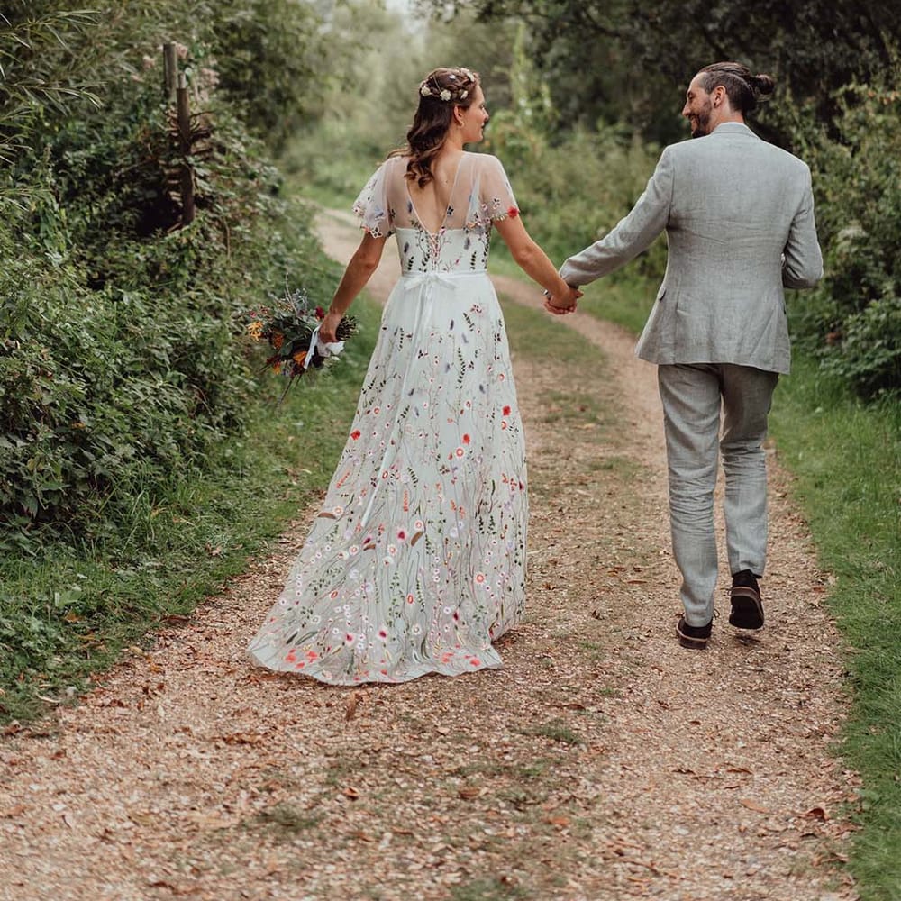 Bride in floral embroidered wedding dress holding hands with groom in grey suit
