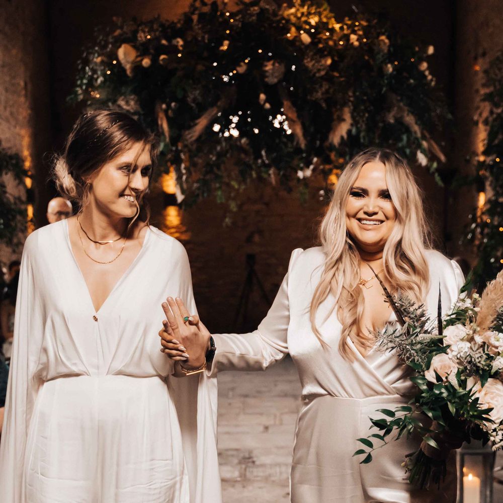 Two brides in jumpsuits at rustic barn wedding white flowers mixed with dried grasses and foliage 
