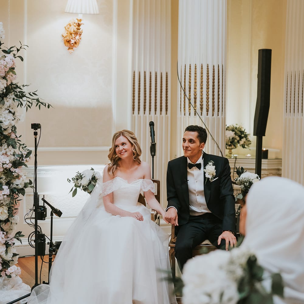 Bride and groom sit holding hands during their wedding ceremony 