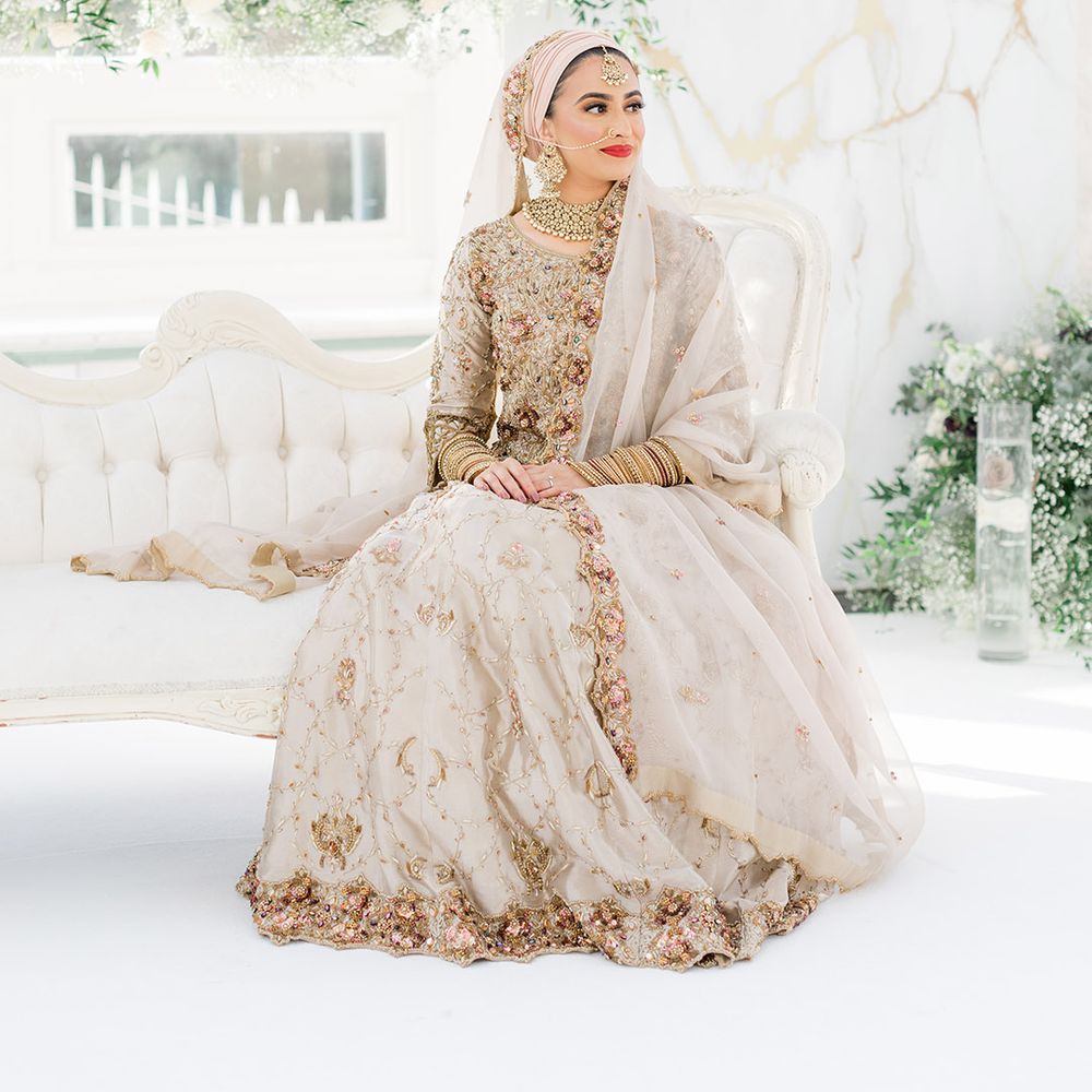 Bride sits on sofa as she wears traditional saree in gold and silver complete with colourful embellishment for Walima ceremony 