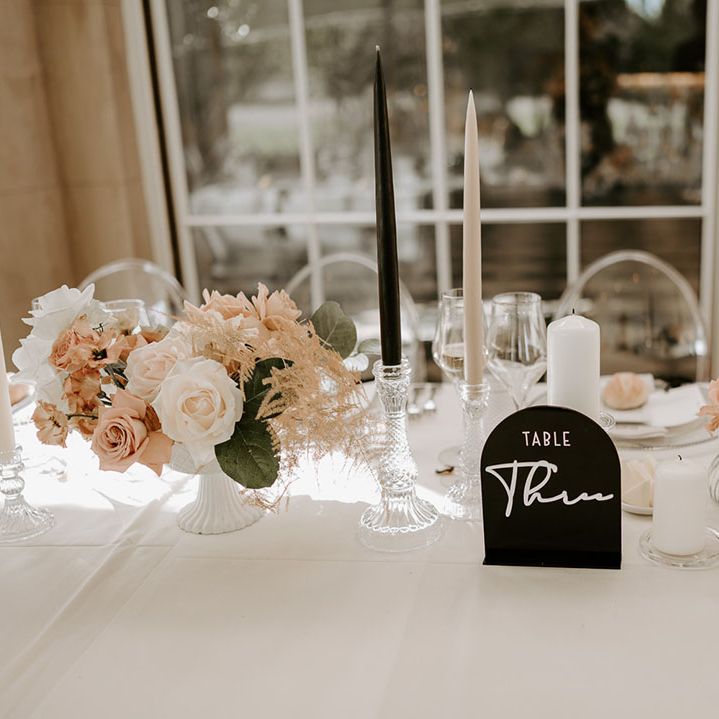 Pale pink and white wedding flower arrangements with a black table name sign and taper candles 