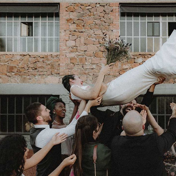 Lisa in pre loved wedding dress is lifted by wedding guests outdoors 
