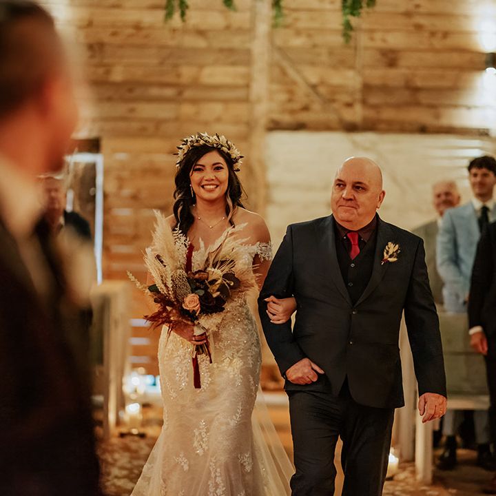 Father of the bride in black suit with red tie walks the bride in a lace off the shoulder wedding dress downtime aisle for autumnal wedding at Milling Barn