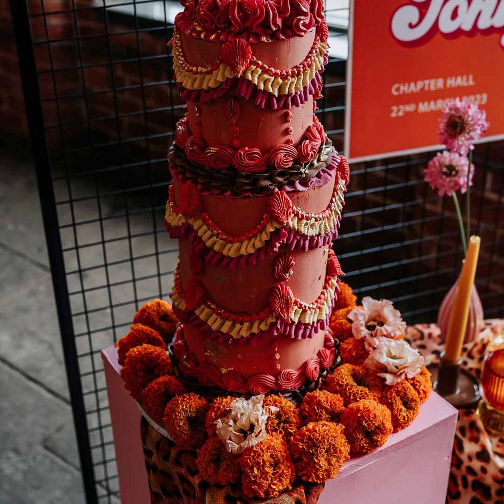Large two tier misshapen pink retro wedding cake with dramatic yellow, deep green, pink and red icon with maraschino cherries on retro geometric wedding cake stand with leopard print wedding drapes 
