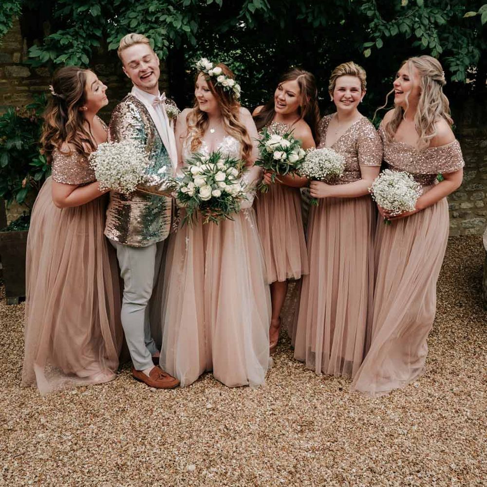 Bride in embellished pink wedding dress standing with bridal party wearing embellished silver sparkly suit and embellished pink off shoulder bridesmaid dresses