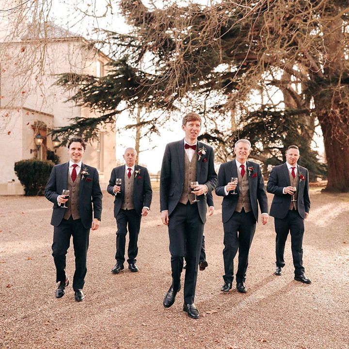 Festive red wine being held by groom and groomsmen in navy suits with grey and red details 