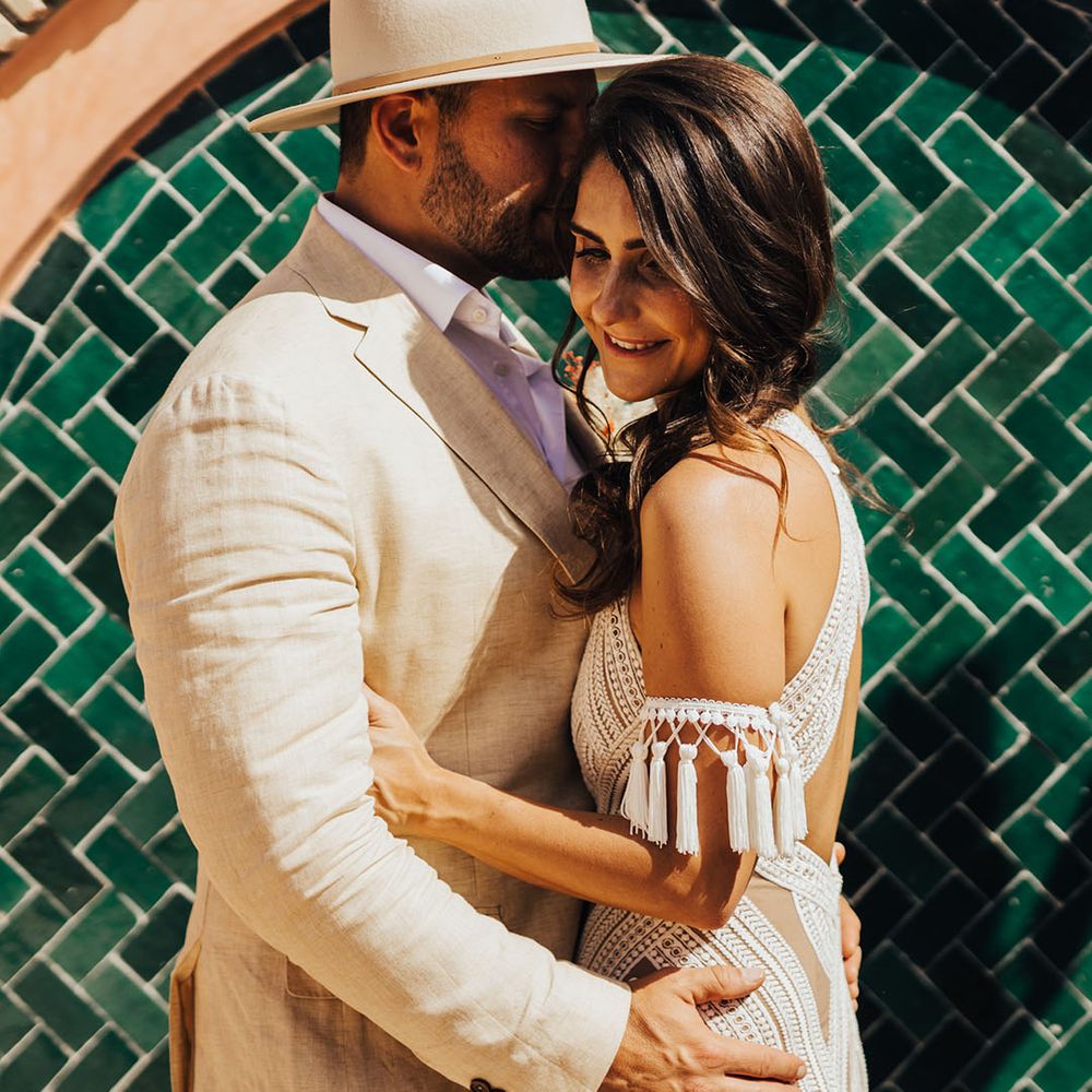 Groom wearing hat embraces the bride for couple photo at boho wedding 