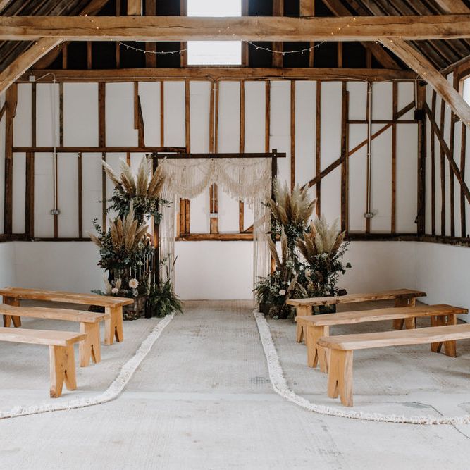 Luxe barn wedding with macramé backdrop and wooden seating and pampas grass