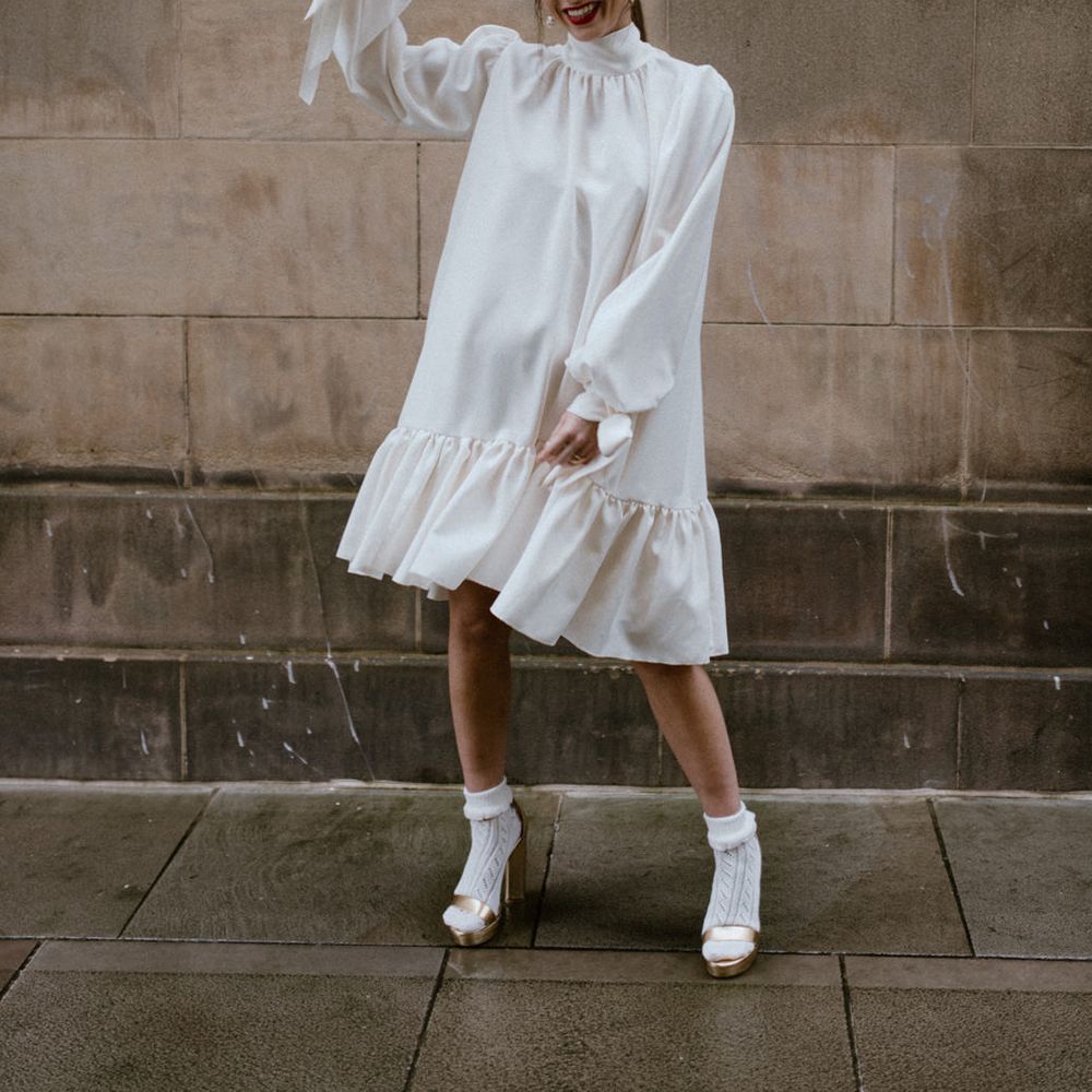 Stylish bride in a high neck silk wedding dress with long sleeve holding up her all white rose bouquet 