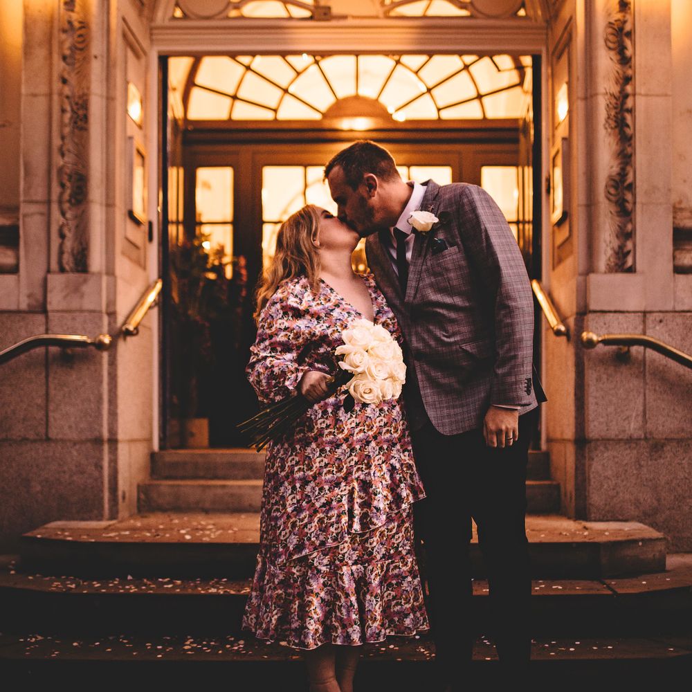 Bride & groom kiss on the steps in front of a brightly lit Chelsea Old Town Hall