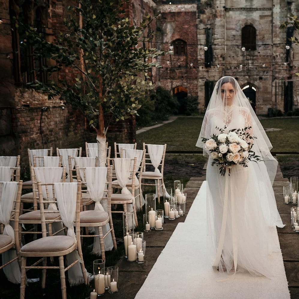 Bride walking down the aisle wearing a wedding veil and holding a rose bouquet 
