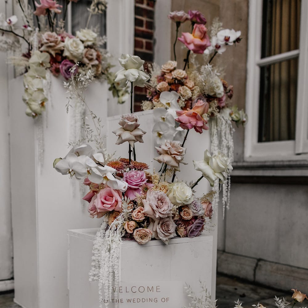 Frosted acrylic wedding welcome sign resting against a white plinth decorated with romantic blush wedding flowers 