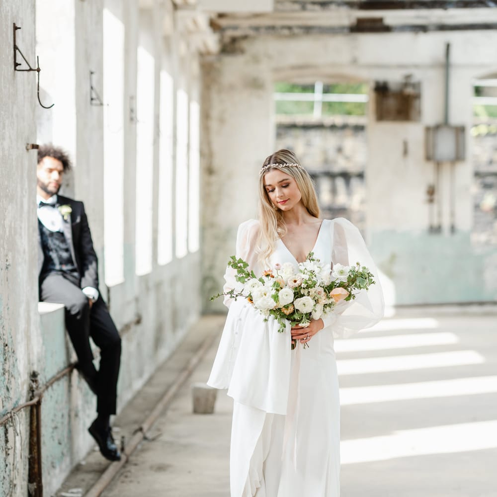 Beautiful bride wearing a dress with puff sleeves holding a white ranunculus, anemone and foliage wedding bouquet 